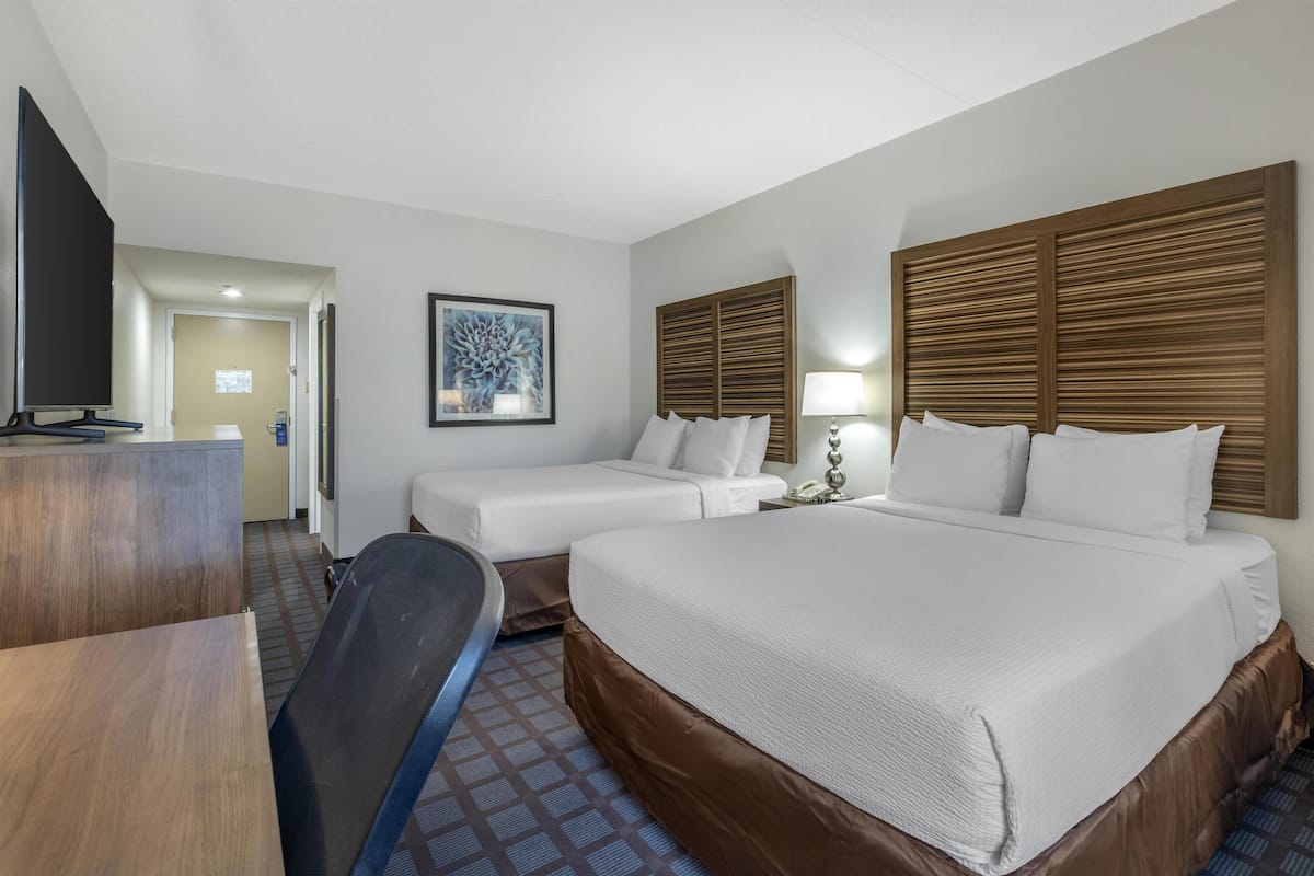 A hotel room with a large bed, two smaller beds, a desk, a TV, and a framed picture on the wall.