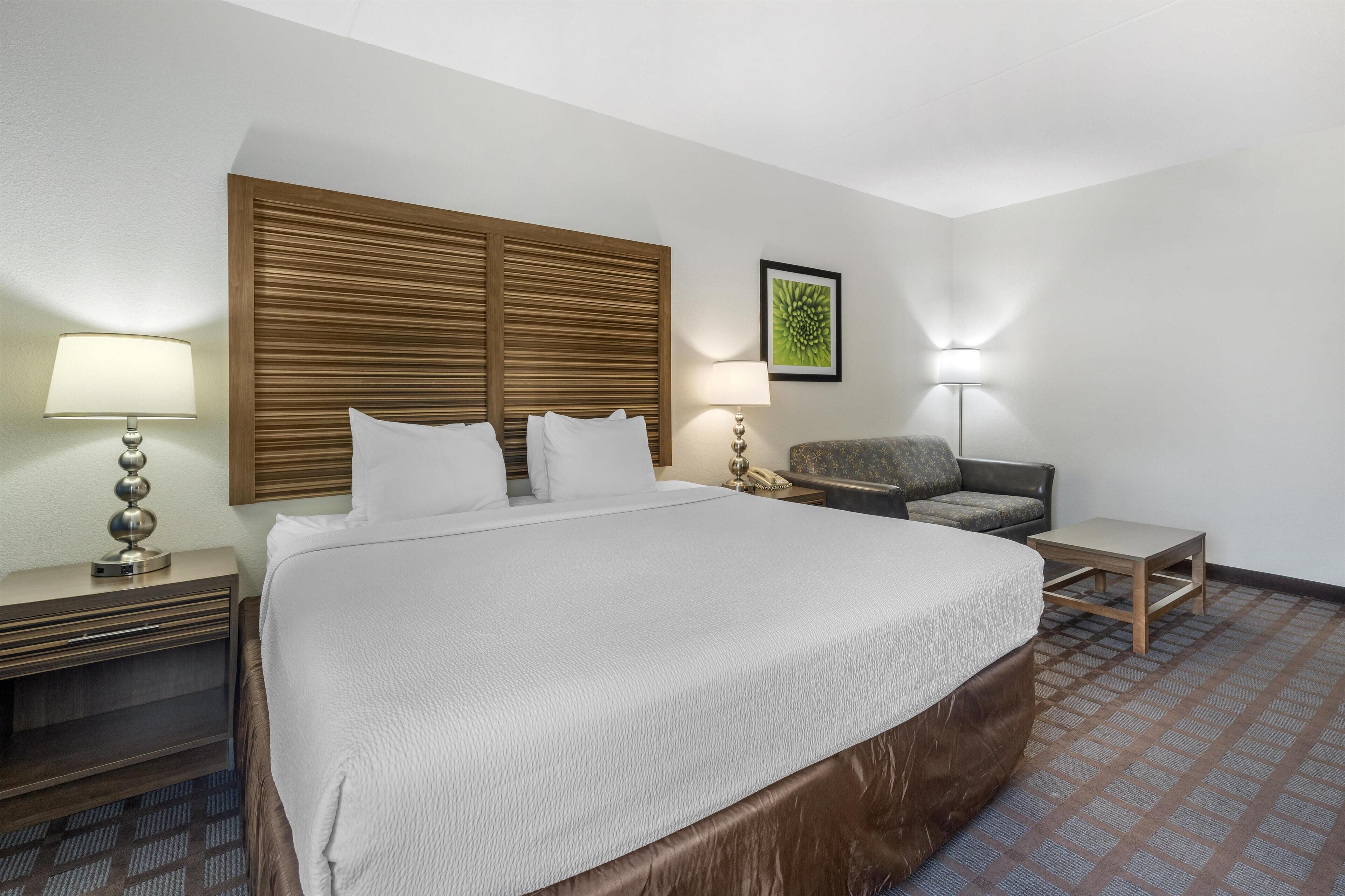A hotel room with a large bed, two bedside tables, a chair, and a small table.