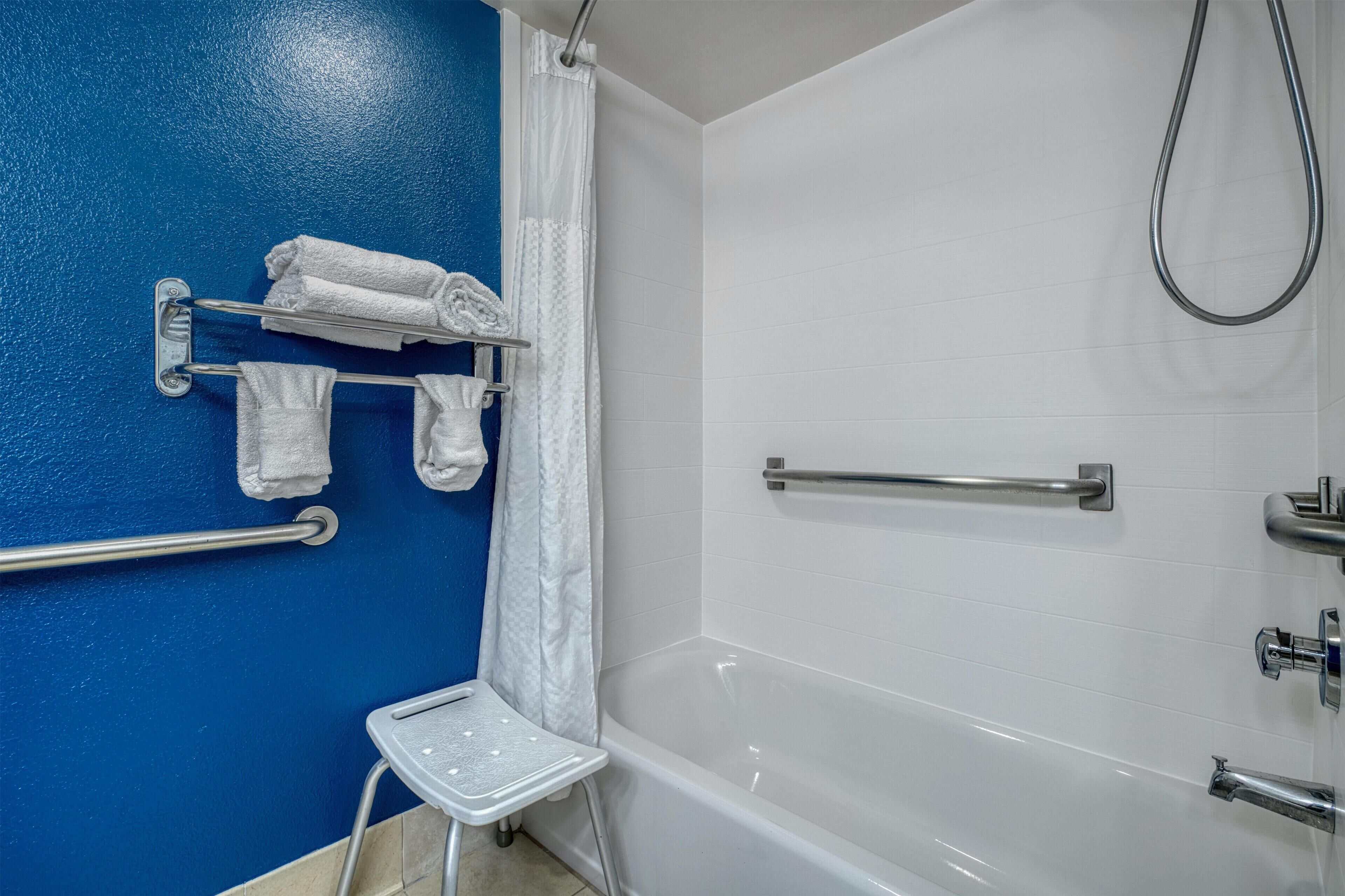 A bathroom with a blue wall, white tiles, a bathtub, a shower, a towel rack with towels, and a small step stool.