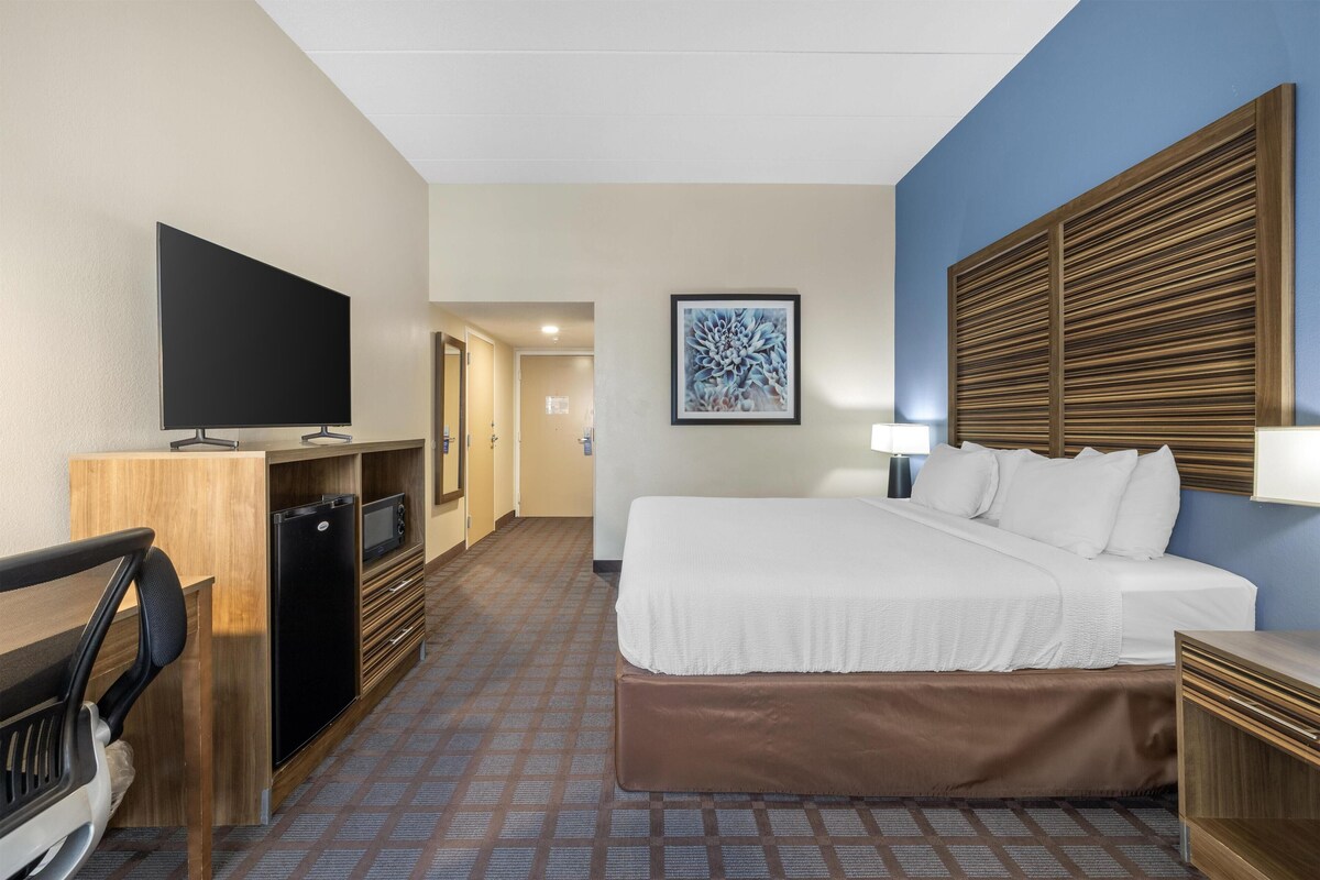 A hotel room with a bed, a desk, a television, and a painting on the wall.