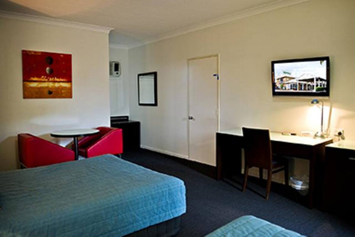 Quarto de hotel com cama, escrivaninha, cadeira, mesinha e televisão.