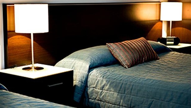 A hotel room with a bed, two bedside tables with lamps, and a headboard. - Gympie Muster Inn (Gympie)