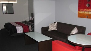 A hotel room with a bed, a sofa, a small table, and a red chair. - Gympie Muster Inn (Gympie)