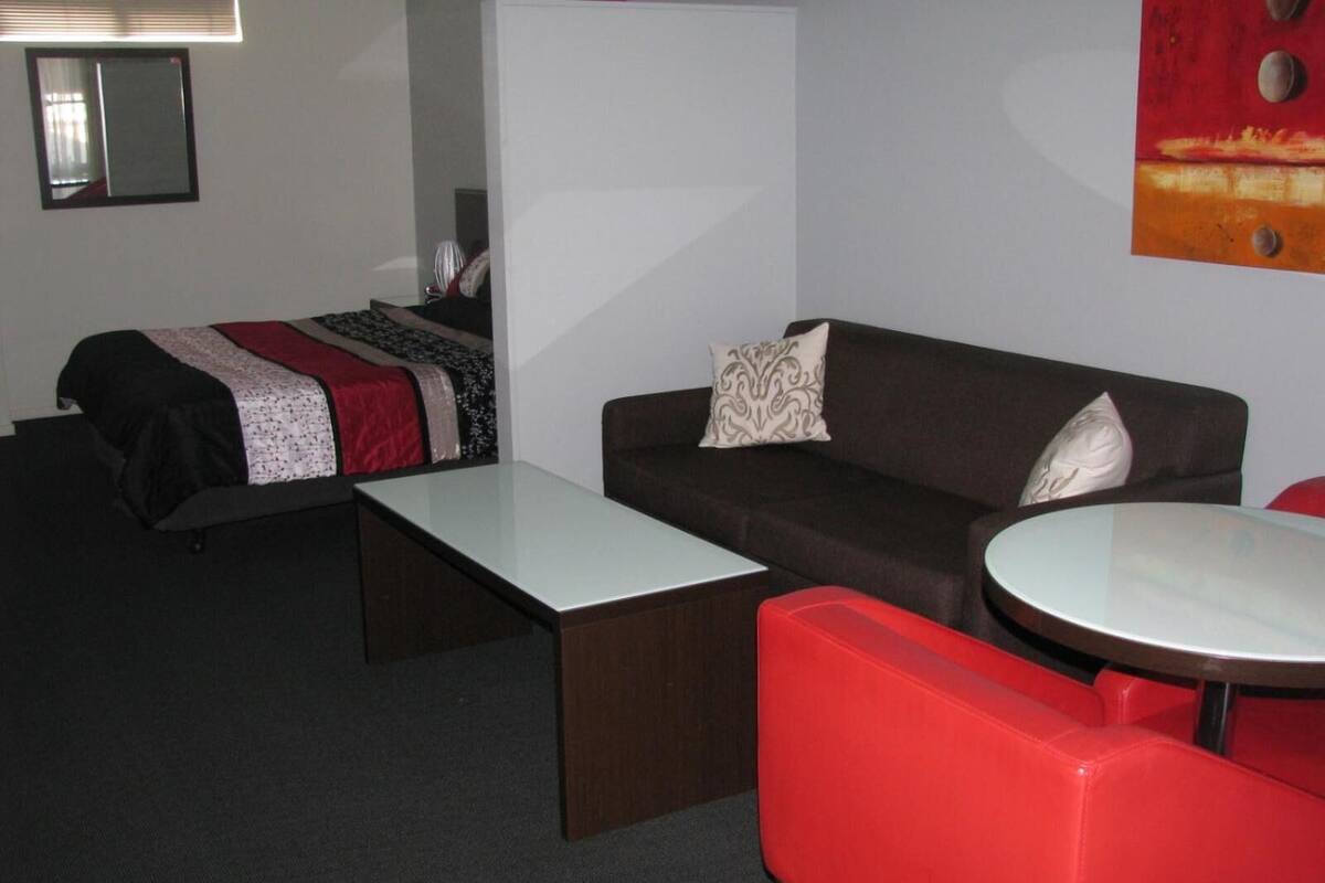 Quarto de hotel com uma cama, um sofá, uma mesinha e uma cadeira vermelha.