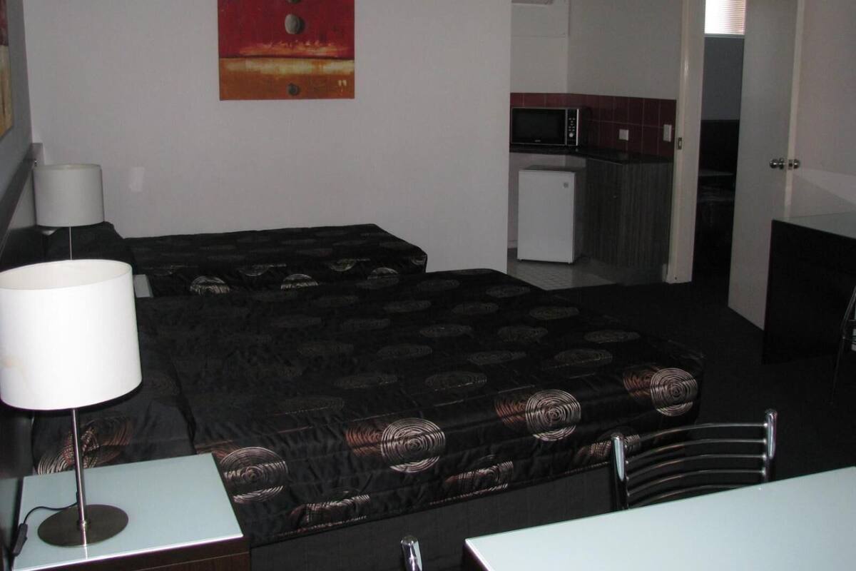 Quarto compacto com cama, escrivaninha, luminária, micro-ondas e geladeira.