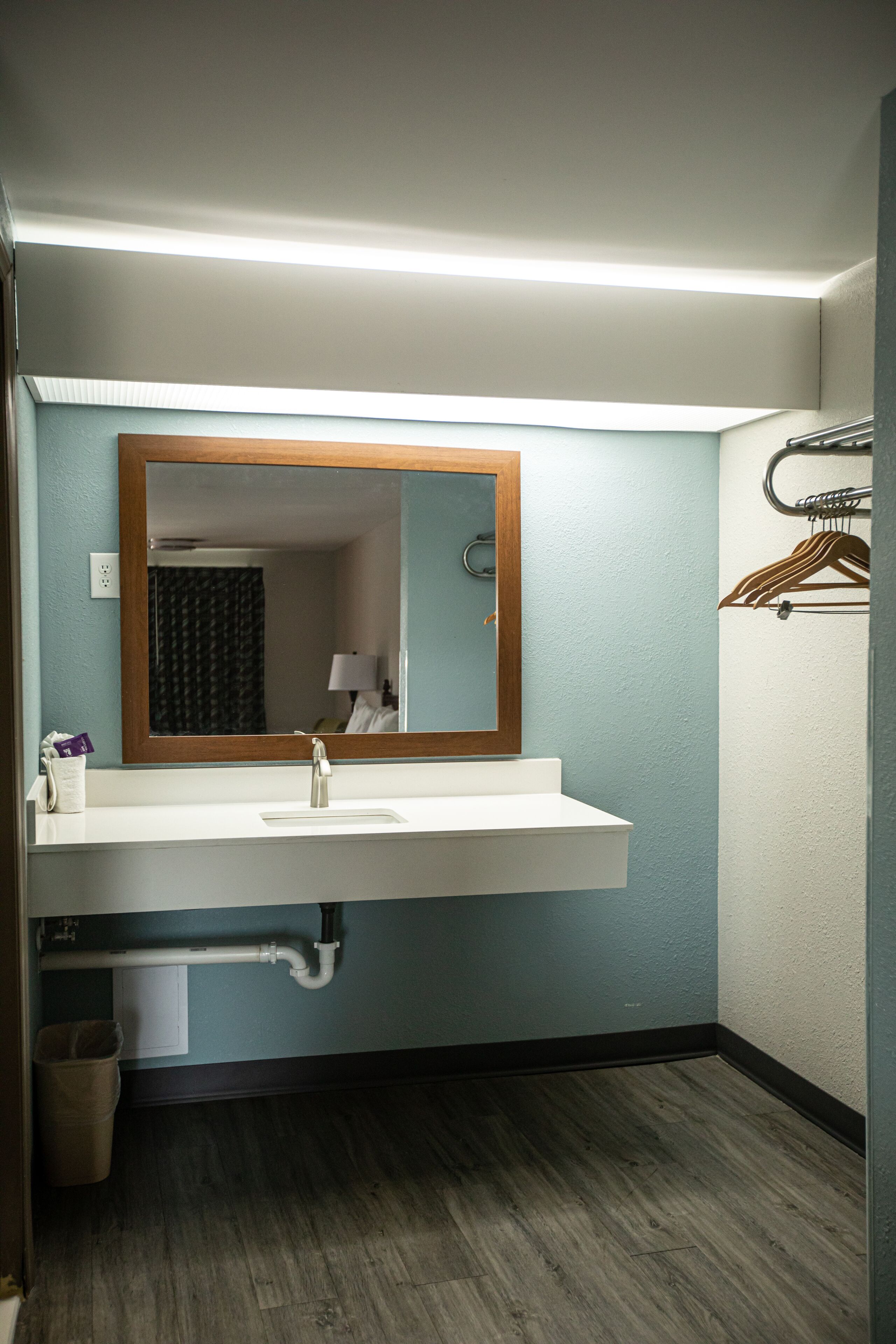 Une salle de bain avec un lavabo blanc, un miroir, un porte-serviettes et un plancher en bois.