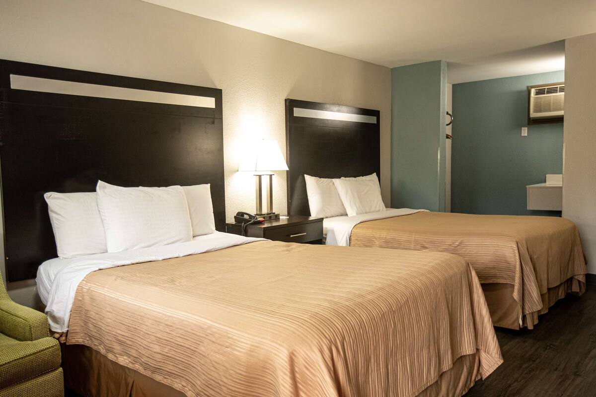 A hotel room with two beds, each with a headboard, a bedside table with a lamp, and a green chair.