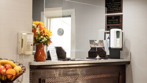 Een receptie met een houten balie, een vaas met bloemen, een fruitmand, een telefoon en een bordje dat aangeeft dat de manager aanwezig is.