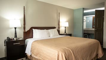 Une chambre d’hôtel avec un grand lit, deux tables de chevet avec des lampes, une commode, un miroir et une porte donnant sur une salle de bain.