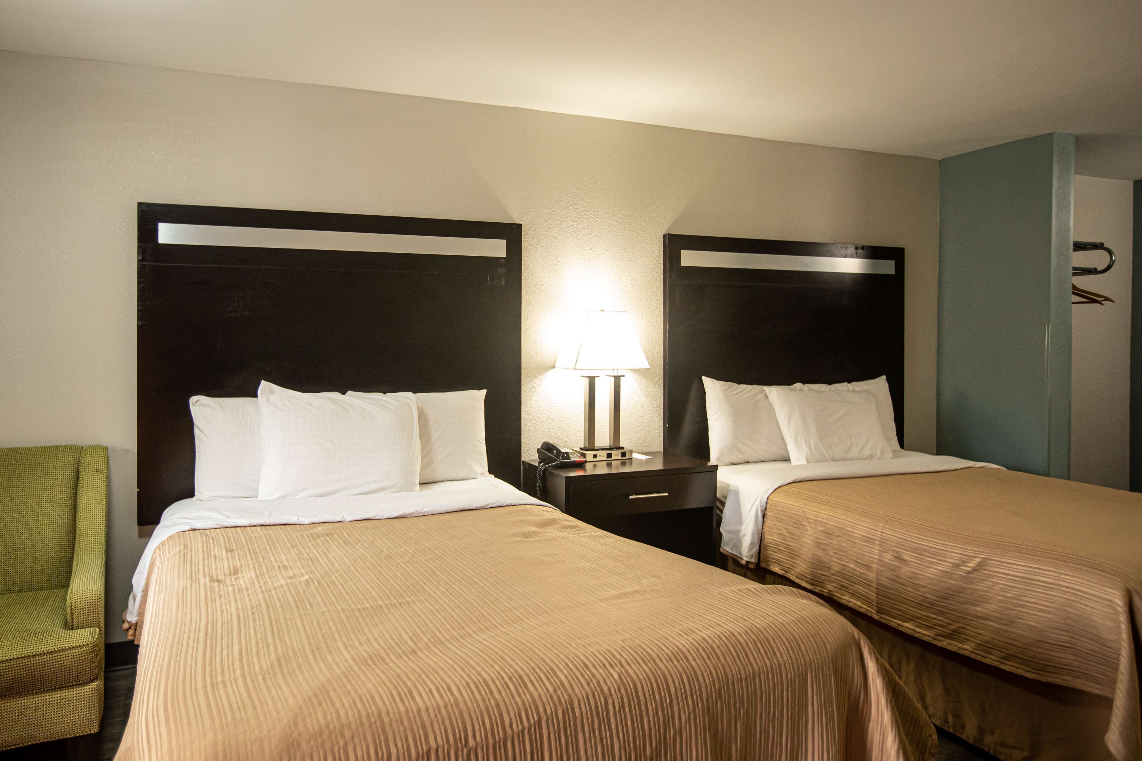 A hotel room with two beds, a nightstand with a lamp, a green chair, and a wardrobe.