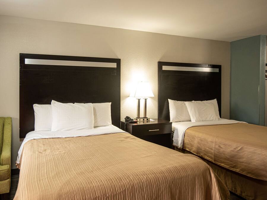 A hotel room with two beds, a nightstand with a lamp, a green chair, and a wardrobe.