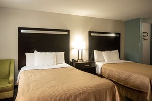 A hotel room with two beds, a nightstand with a lamp, a green chair, and a wardrobe.