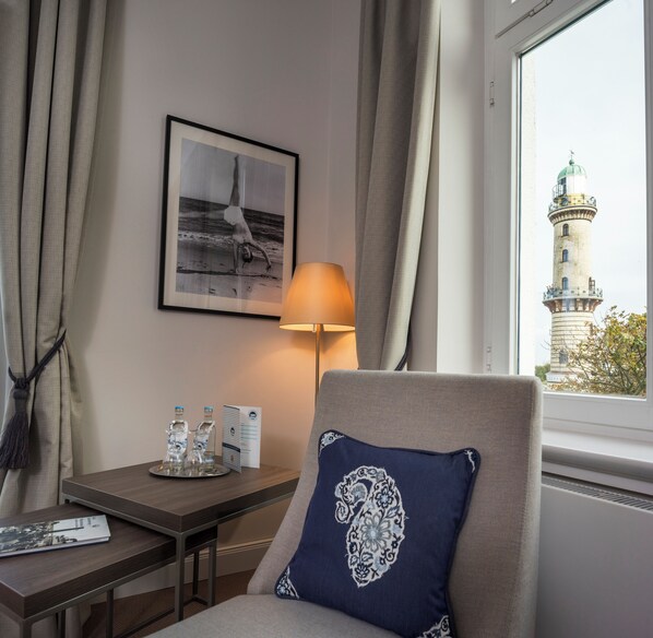 A hotel room with a bed, a desk with a lamp, a framed photo on the wall, and a view of a lighthouse through the window. - Hotel Am Leuchtturm (Rostock)