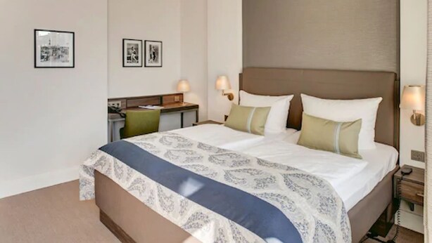 Una habitación de hotel con una cama grande, mesitas de noche, lámparas y cuadros en la pared.