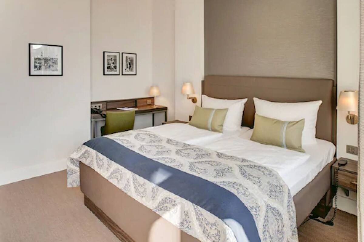 A hotel room with a large bed, bedside tables, lamps, and framed pictures on the wall.