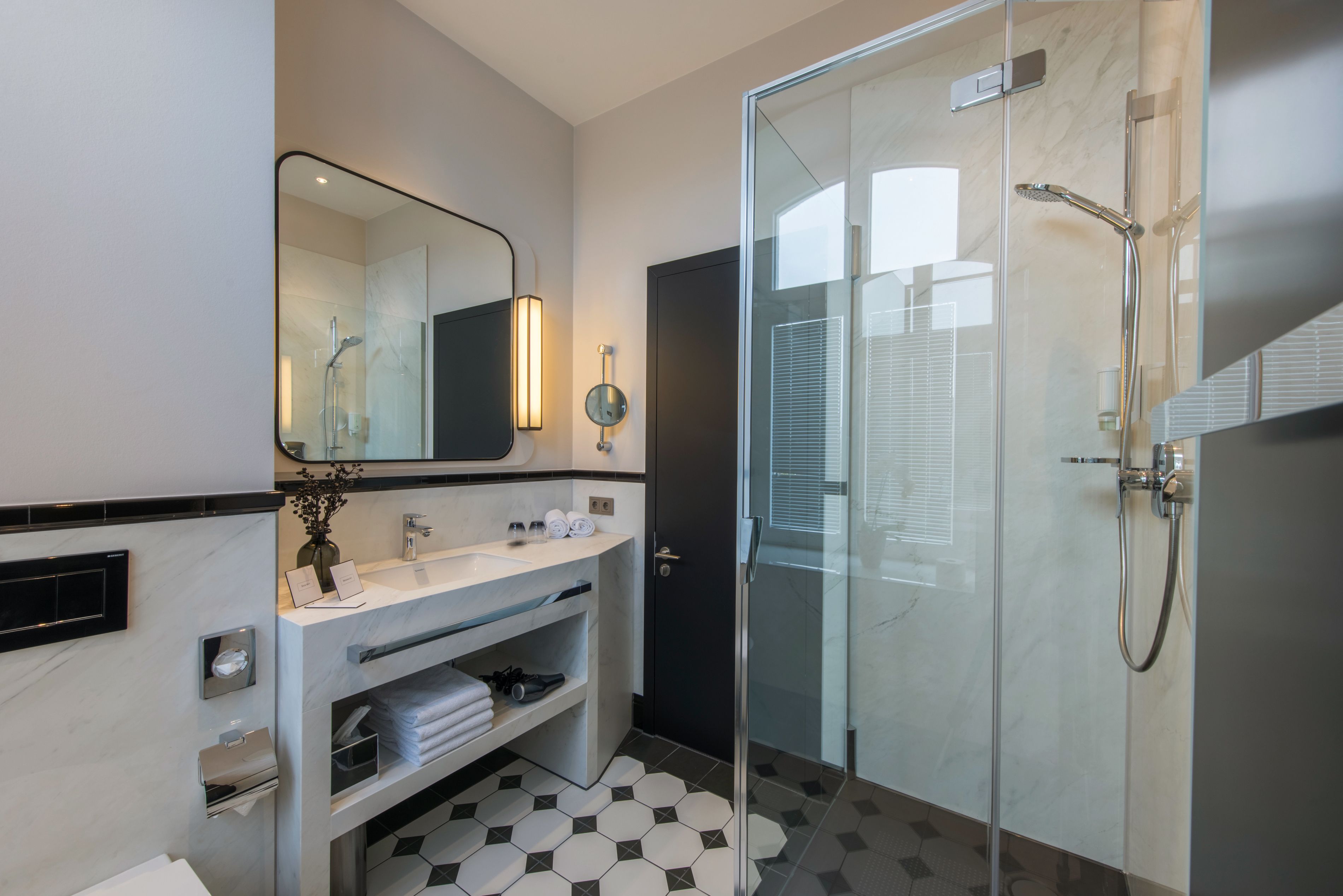 A modern bathroom with a glass shower enclosure, a marble vanity, and a large mirror with wall-mounted lights.