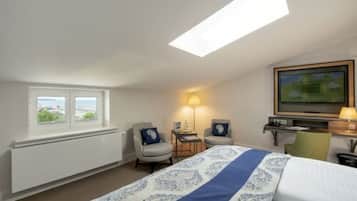 Ein Hotelzimmer mit einem Bett, zwei Sesseln, einem Schreibtisch, einem Fernseher und einem Fenster mit Blick.
