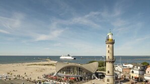 Un pueblo costero con un faro destacado, un edificio moderno con forma curva y una playa.