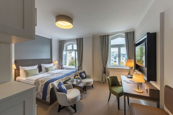 A hotel room with a bed, two chairs, a desk, a TV, and large windows. - Hotel Am Leuchtturm (Rostock)