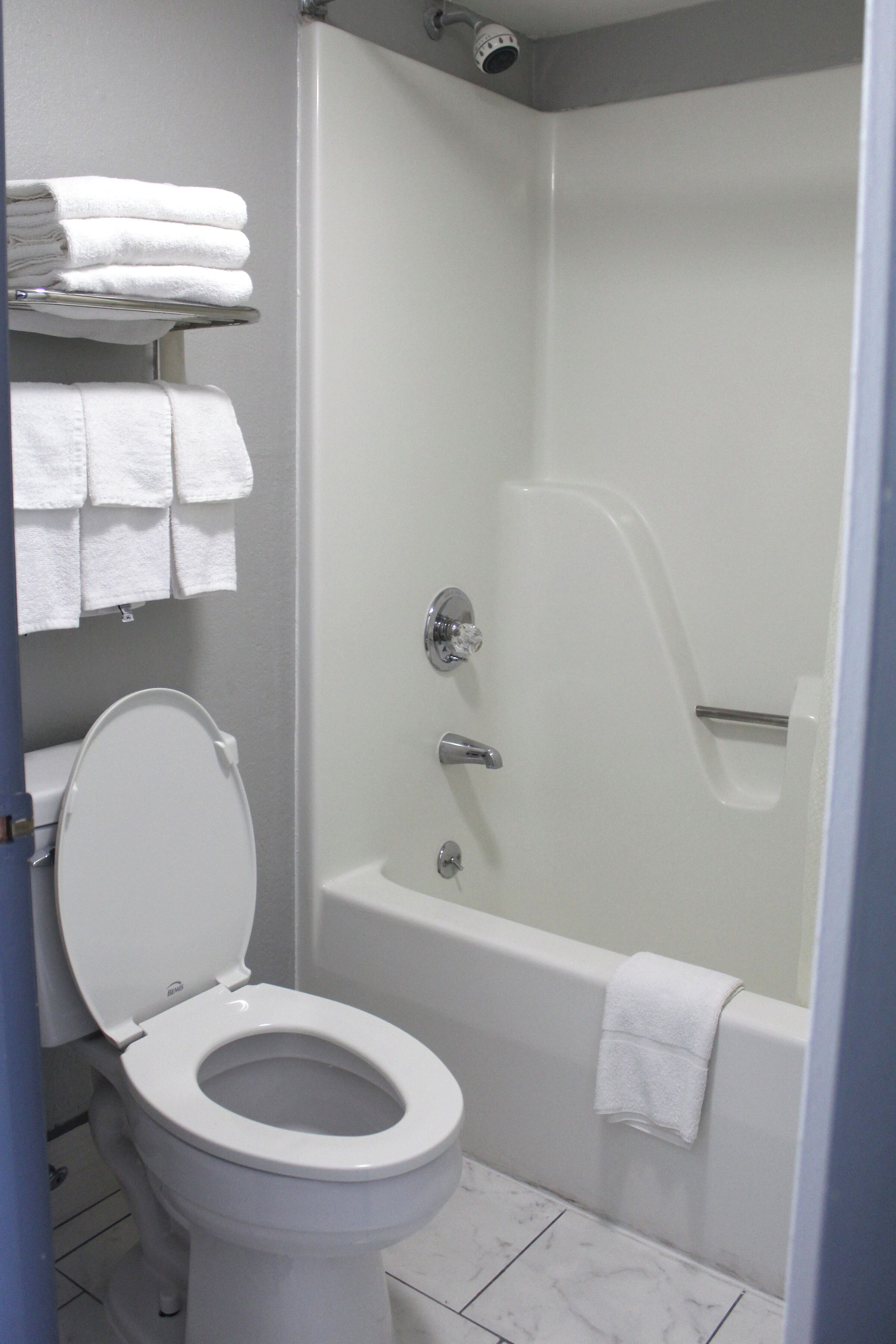 Un baño con inodoro, bañera y ducha. Hay toallas apiladas en un escurreplatos.