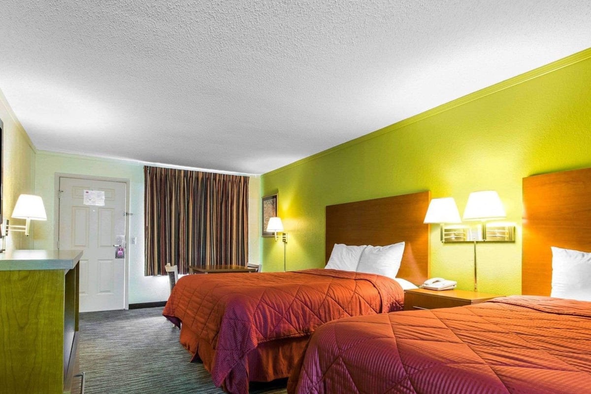 A hotel room with two beds, a desk, a chair, a door, and a curtain.