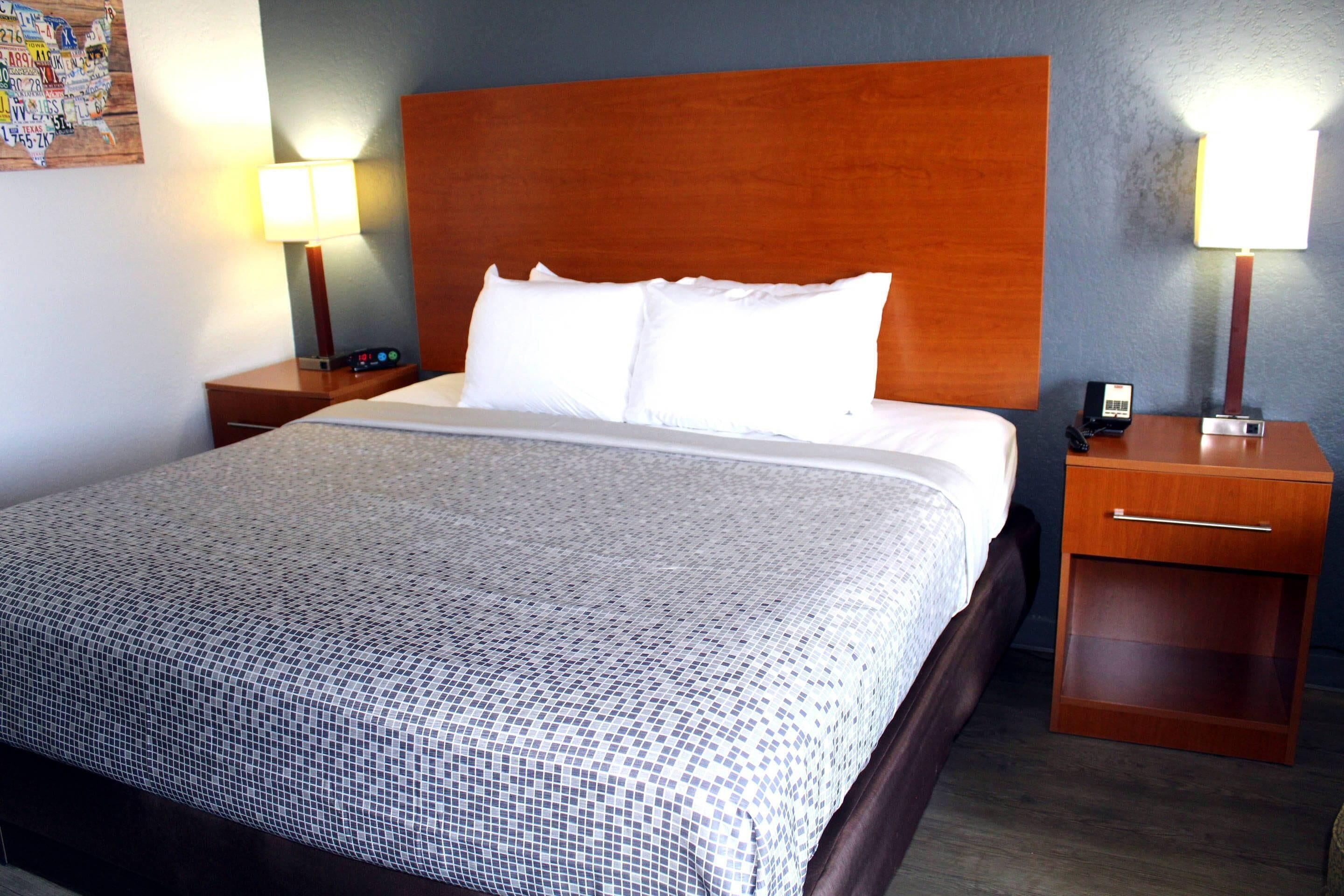 A neatly made bed with a patterned bedspread, wooden headboard, and two bedside tables with lamps and a phone.