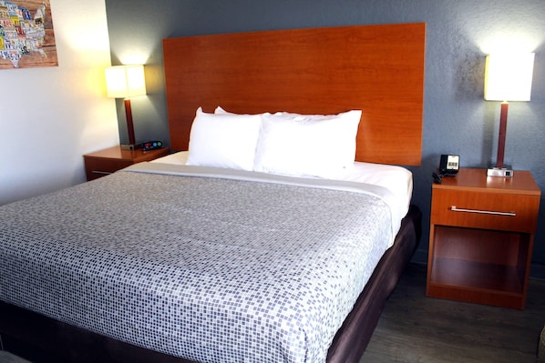 Una cama bien hecha con una colcha estampada, cabecera de madera y dos mesitas de noche con lámparas y un teléfono.