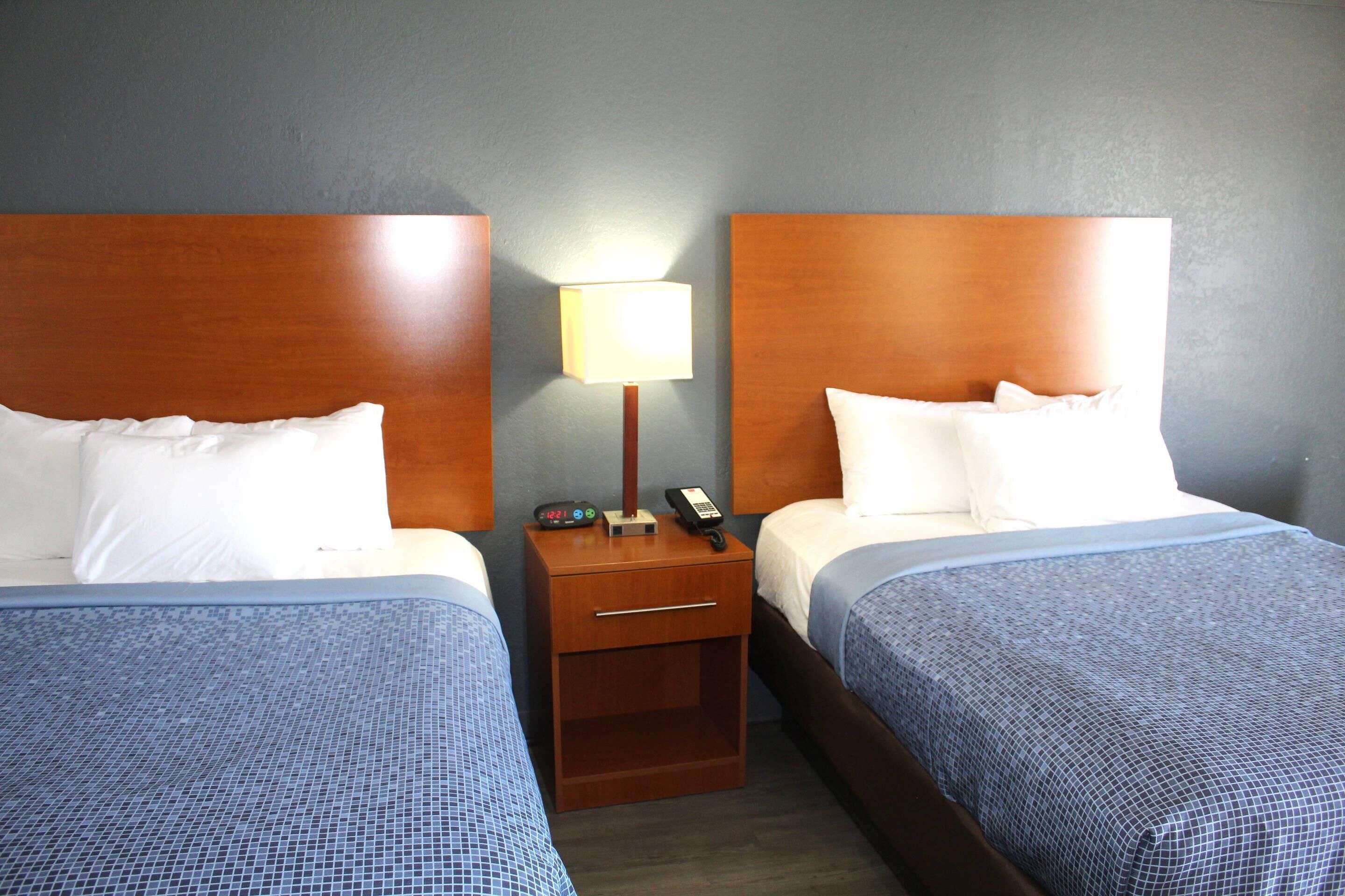 Habitación de hotel con dos camas, cada una con cabecero de madera, una mesita de noche con lámpara y teléfono.