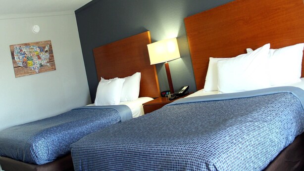 A hotel room with two beds, a wooden headboard, a nightstand with a lamp, and a wall decoration. - Econo Lodge Franklin South (Franklin)