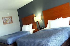 Habitación de hotel con dos camas, cabecero de madera, mesita de noche con lámpara y un adorno en la pared.