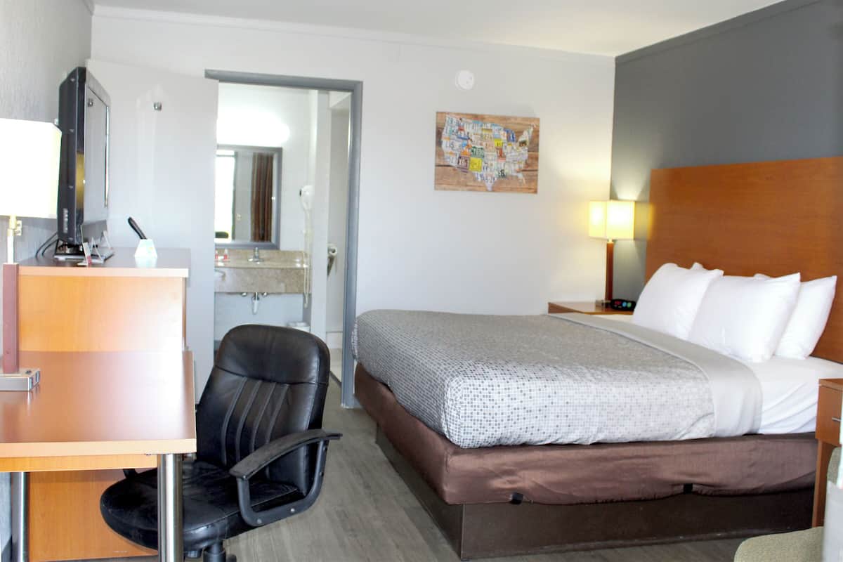 A hotel room with a bed, desk, chair, and a map on the wall.