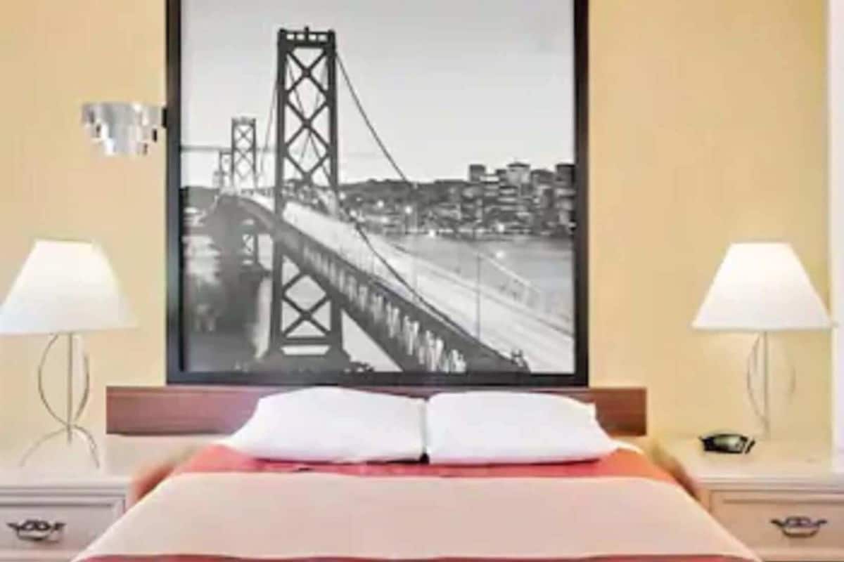 A hotel room with a bed, two bedside lamps, a framed picture of a bridge, and a nightstand with a lamp.