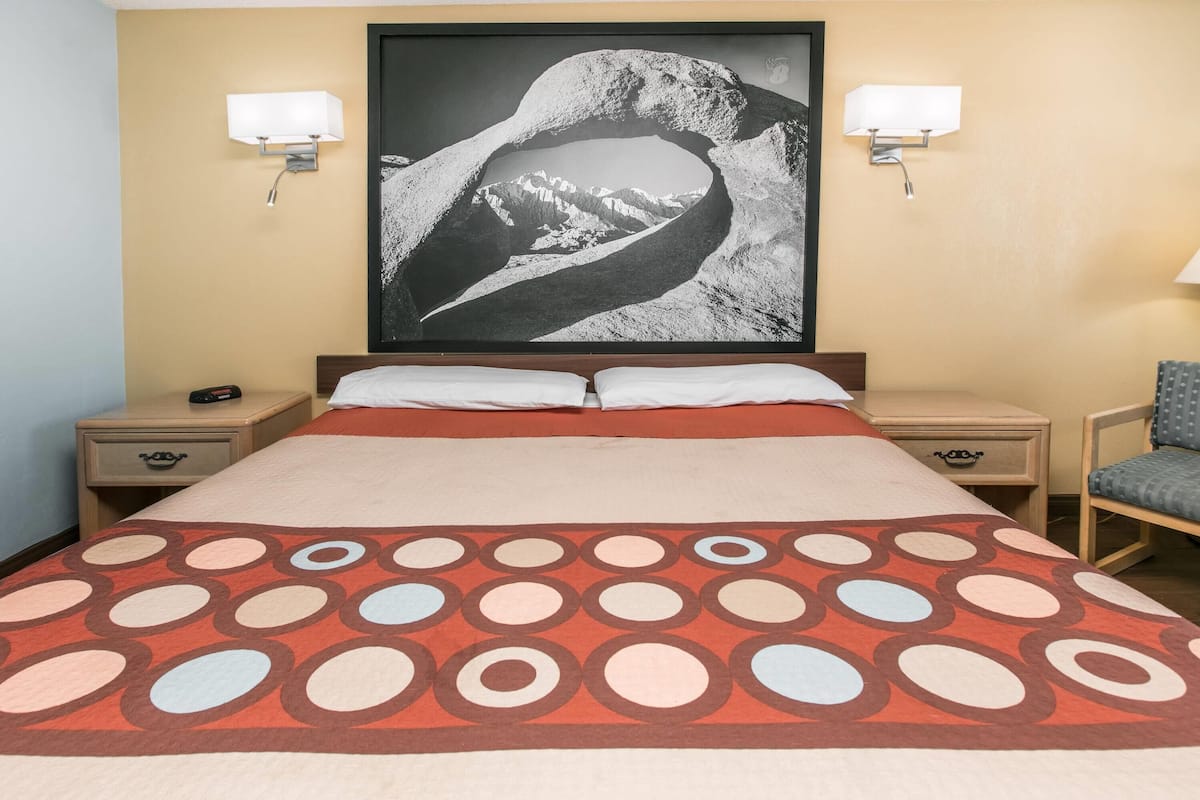 A hotel room with a bed, two nightstands, a chair, and a large framed picture on the wall.
