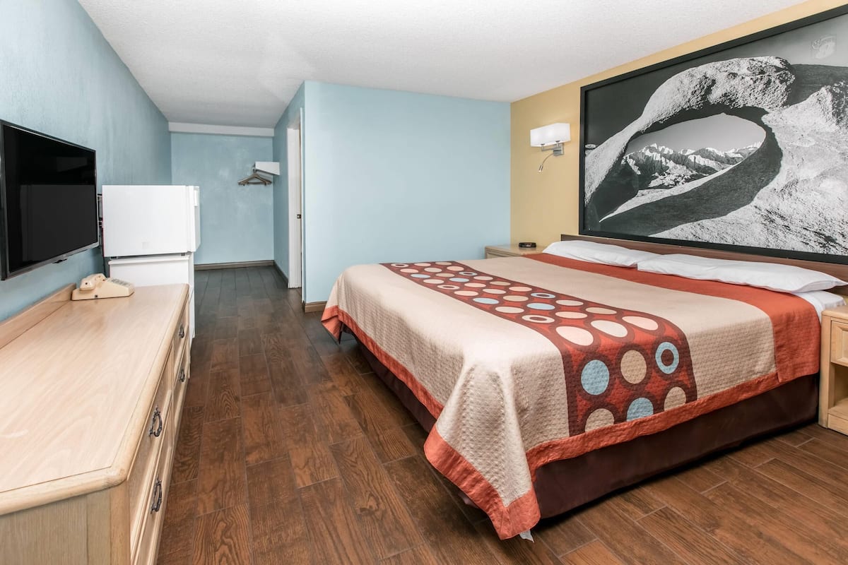 A hotel room with a bed, a television, a refrigerator, and a painting on the wall.