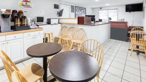 Un área de desayuno con sillas y mesas de madera, una máquina de café y una barra con un panel de menú.