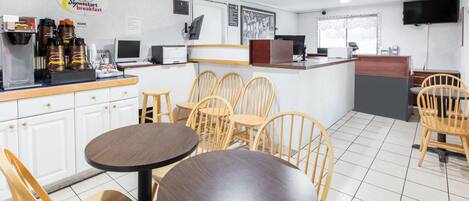 Un área de desayuno con sillas y mesas de madera, una máquina de café y una barra con un panel de menú.