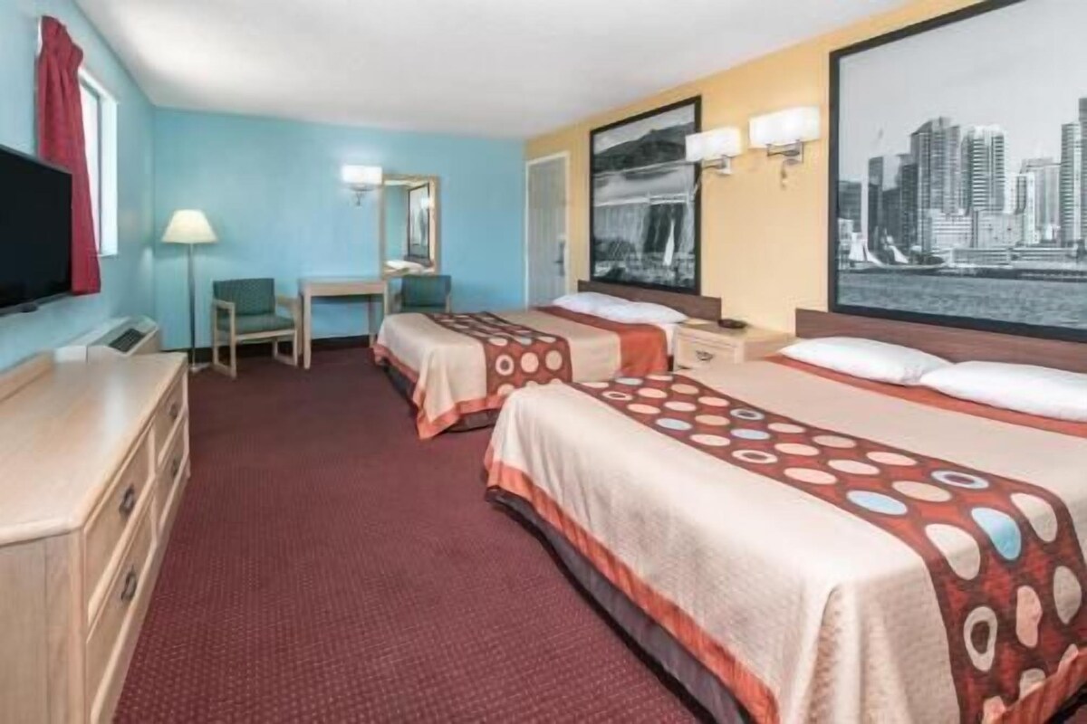 Habitación de hotel con dos camas, un escritorio, una silla, un televisor y vistas a la ciudad.