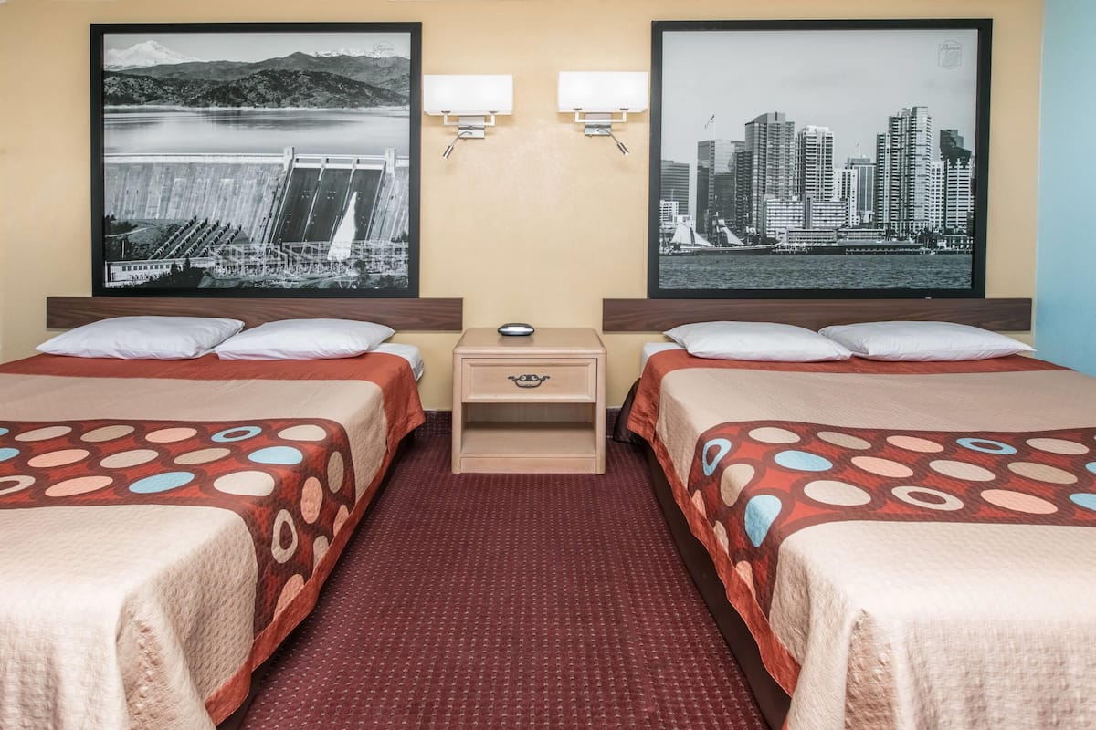 A hotel room with two beds, a nightstand, and two wall-mounted lamps.