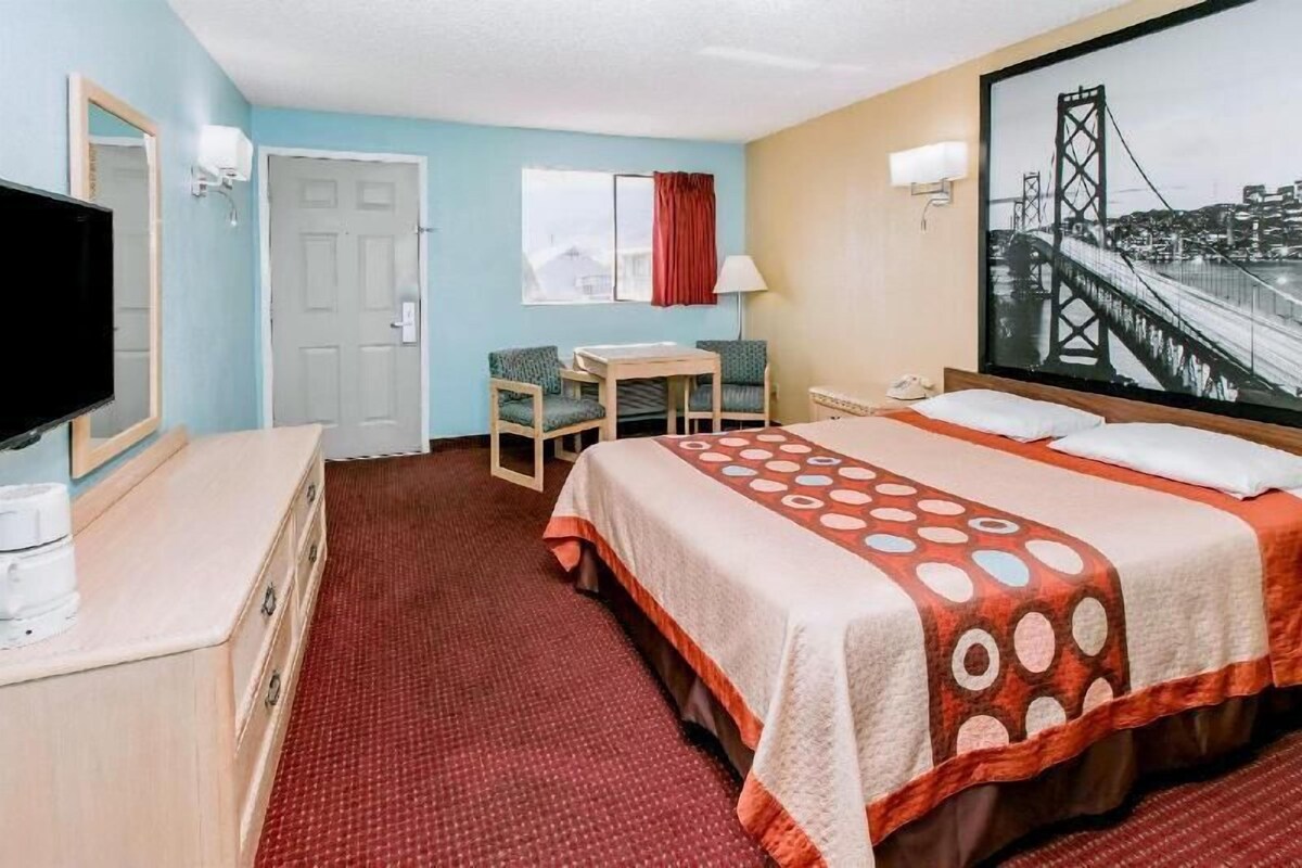 Una habitación de hotel con cama, escritorio, silla, televisor y un ventanal grande.