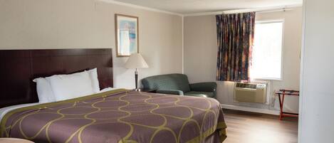 Quarto de hotel com uma cama grande, uma cadeira, uma mesa, janela com cortinas e aparelho de ar condicionado.