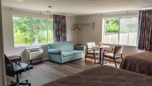 Ein Hotelzimmer mit einer Sitzecke, einem Esstisch mit Stühlen, einem Schreibtisch mit Stuhl und großen Fenstern mit Vorhängen.
