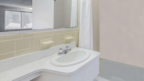 Ein Badezimmer mit einem weißen Waschbecken, einem Spiegel und einem Fenster mit Blick auf ein Haus.