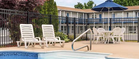 A swimming pool area with lounge chairs and a table, surrounded by a fence and trees.