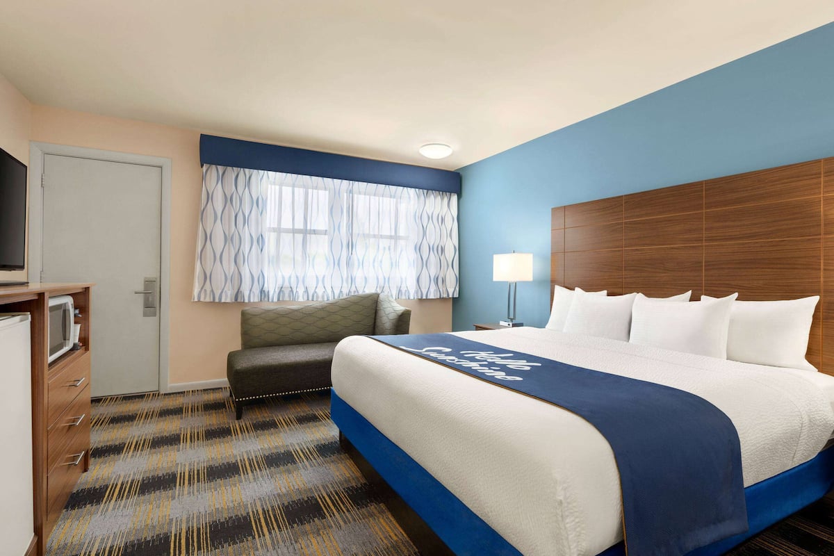 Habitación de hotel con una cama grande, un escritorio con televisor, una ventana con cortinas estampadas y una pared azul de acento.