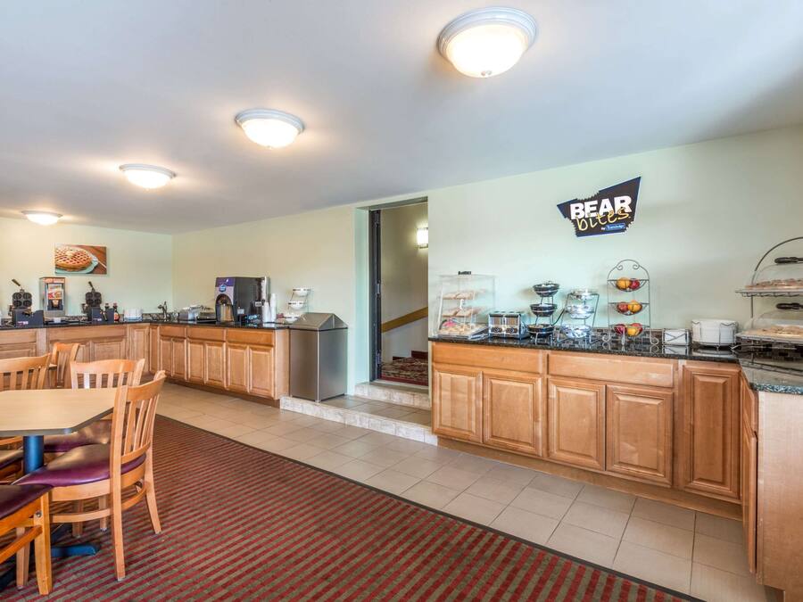 A kitchen with wooden cabinets, a dining area with chairs, a coffee station, and a sign that reads "BEAR OLEO".
