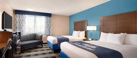 A hotel room with two beds, a desk, a TV, and a window with curtains.