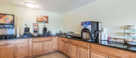 A kitchen with a coffee station, a waffle maker, and a pizza display.