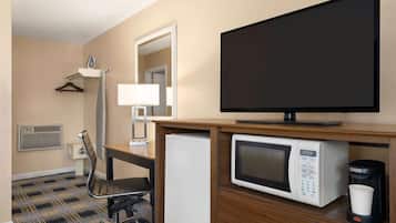 A hotel room with a flat-screen TV, a microwave, a coffee maker, a desk with a chair, a hanging coat rack, and a mirror.