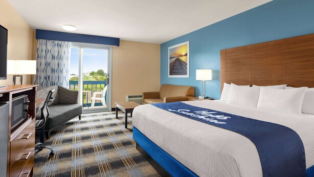 A hotel room with a large bed, a desk, a chair, a TV, and a view of the outdoors. - Days Inn by Wyndham Middletown/Newport Area (Middletown)
