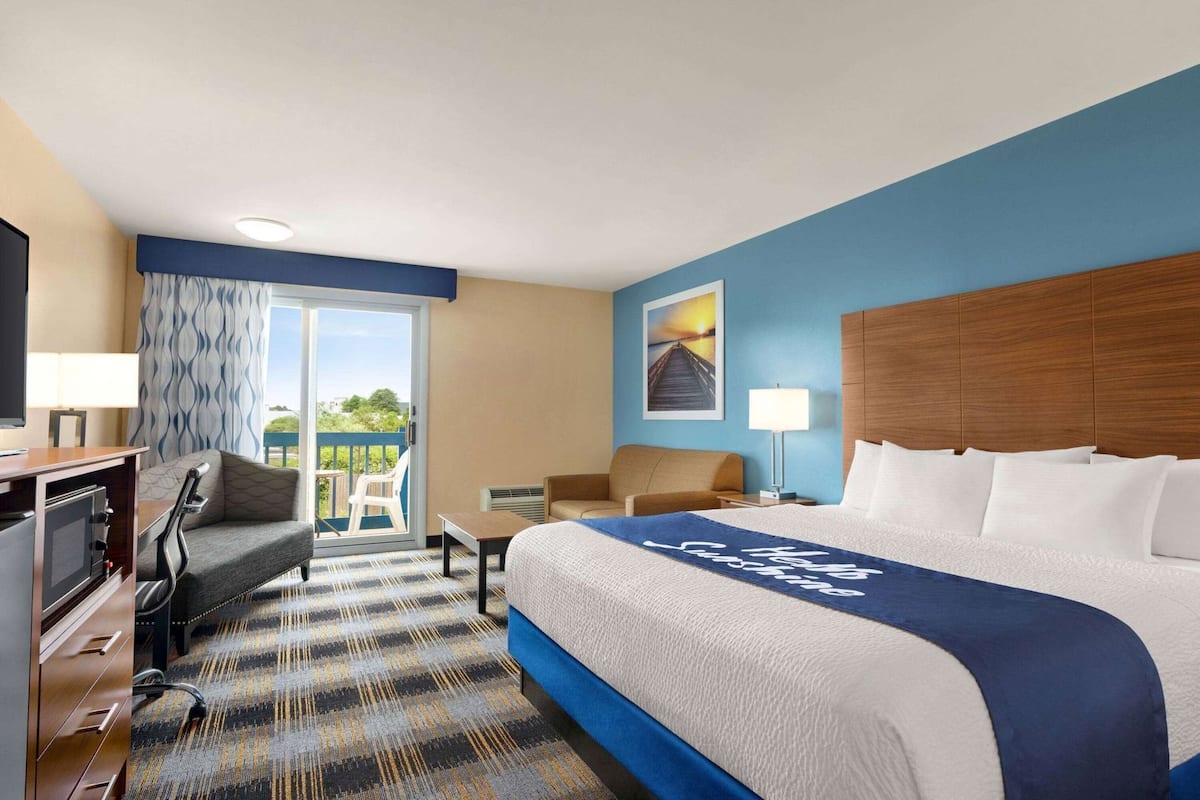 Habitación de hotel con una cama grande, un escritorio con computadora, una silla, un sofá y un balcón con vistas.